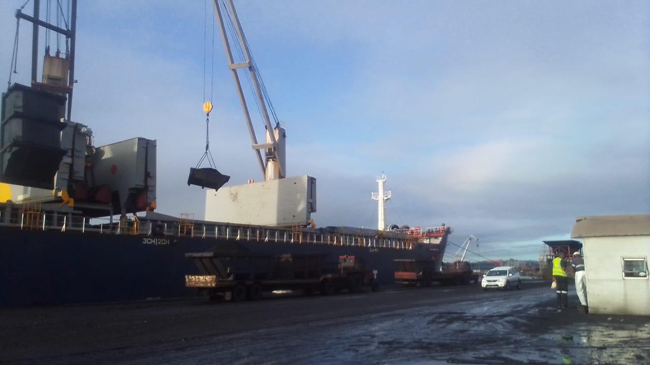 Port crane lifting heavy cargo next to bulk vessel